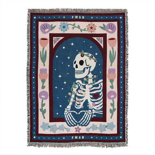 A colorful throw blanket featuring a graphic design with a skeleton, floral patterns, and the text 'FWAB'. The blanket has a decorative fringe on the edges.