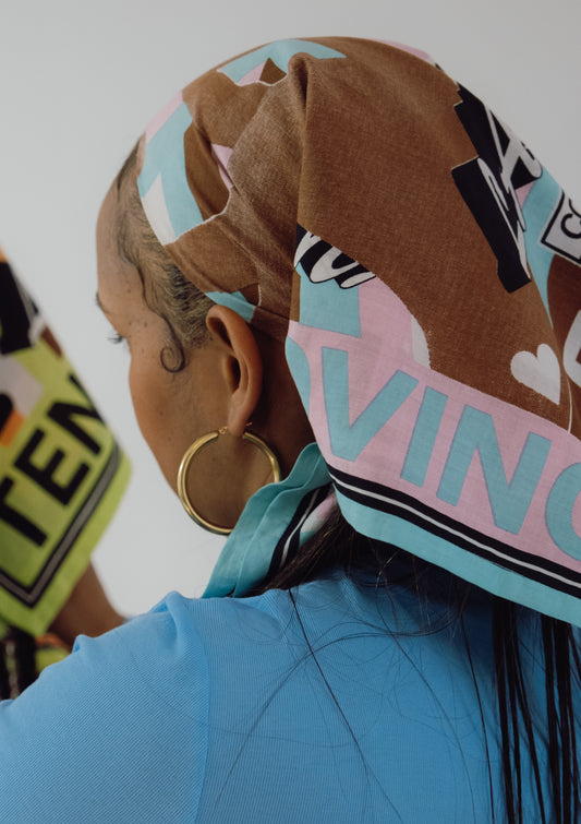 Person wearing a colorful headscarf with text and patterns, partially obscuring their face.