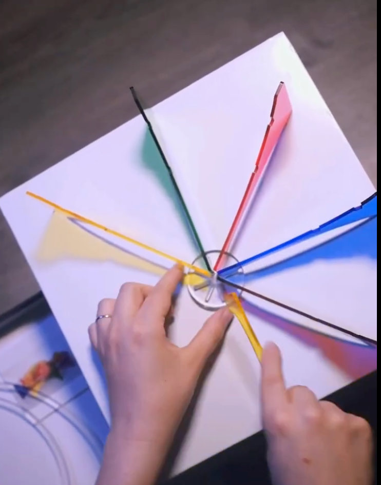 Colorful pieces arranged in a circular pattern on a white surface with hands 