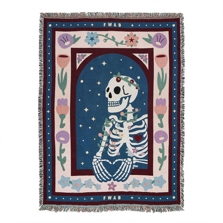 A colorful throw blanket featuring a graphic design with a skeleton, floral patterns, and the text 'FWAB'. The blanket has a decorative fringe on the edges.
