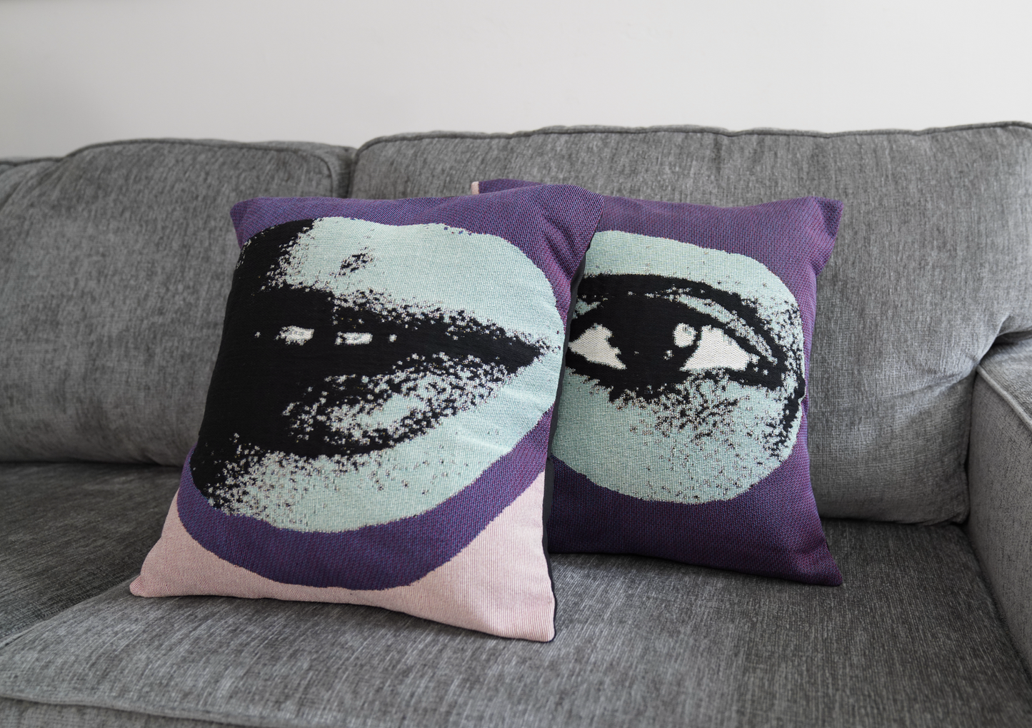 Two decorative pillows with face designs on a gray couch.