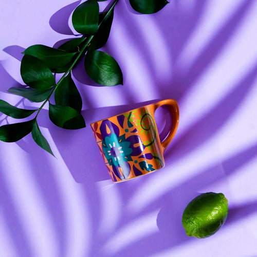 Colorful mug with abstract design on a purple fabric background with leaves and a lime.