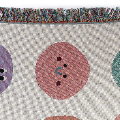 Close-up of a multicolored throw blanket with a pattern of dots in various sizes and colors, including red, blue, purple, and green, with a fringed edge.