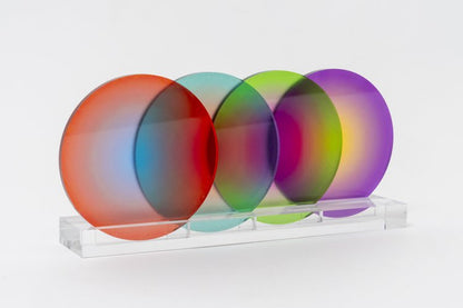 A set of four gradient color coasters in red, orange, yellow, and purple, displayed on a clear stand.