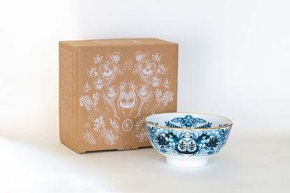 A ceramic bowl with blue floral illustrations, accompanied by a cardboard box with similar designs.