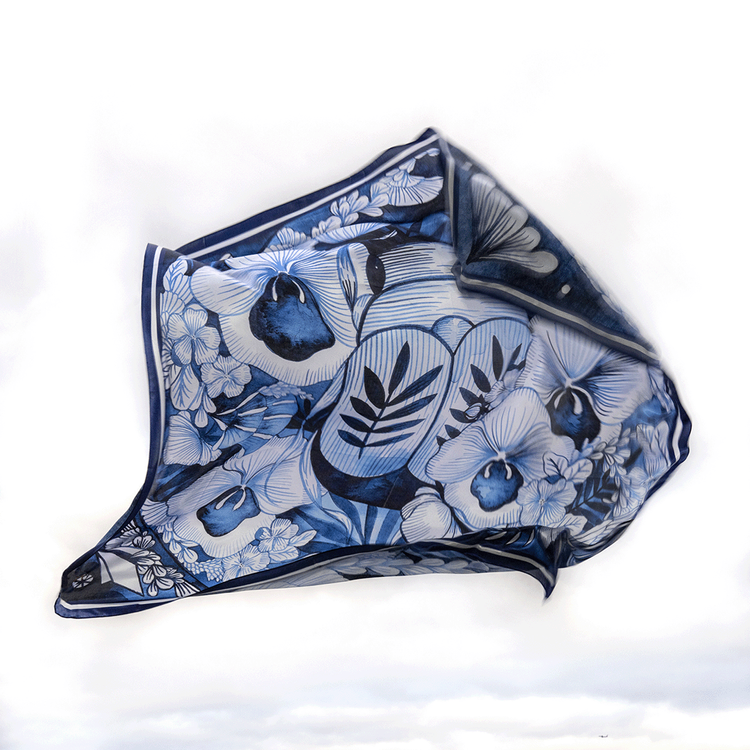 A silk scarf with a floral and mythical creature pattern in shades of blue and white.