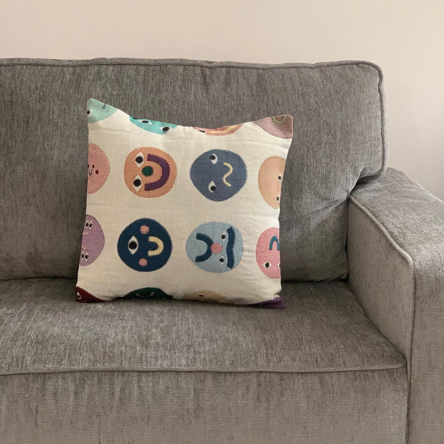 Decorative pillow with smiley face patterns on a gray sofa.