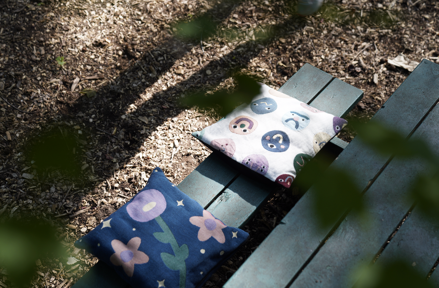 Two decorative pillows on a wooden bench outdoors.