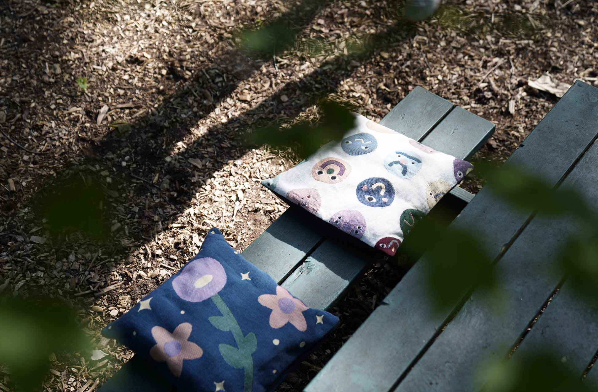 Two decorative pillows on a wooden bench outdoors.