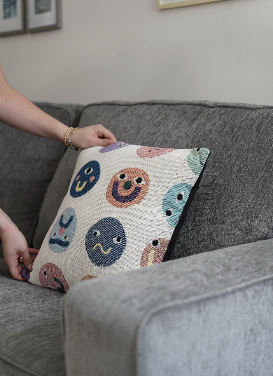Person holding a pillow with colorful face patterns on a gray couch.