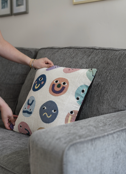 Person holding a pillow with colorful face patterns on a gray couch.