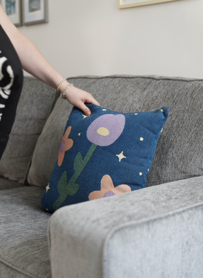 Person holding a decorative pillow with floral design on a gray couch.