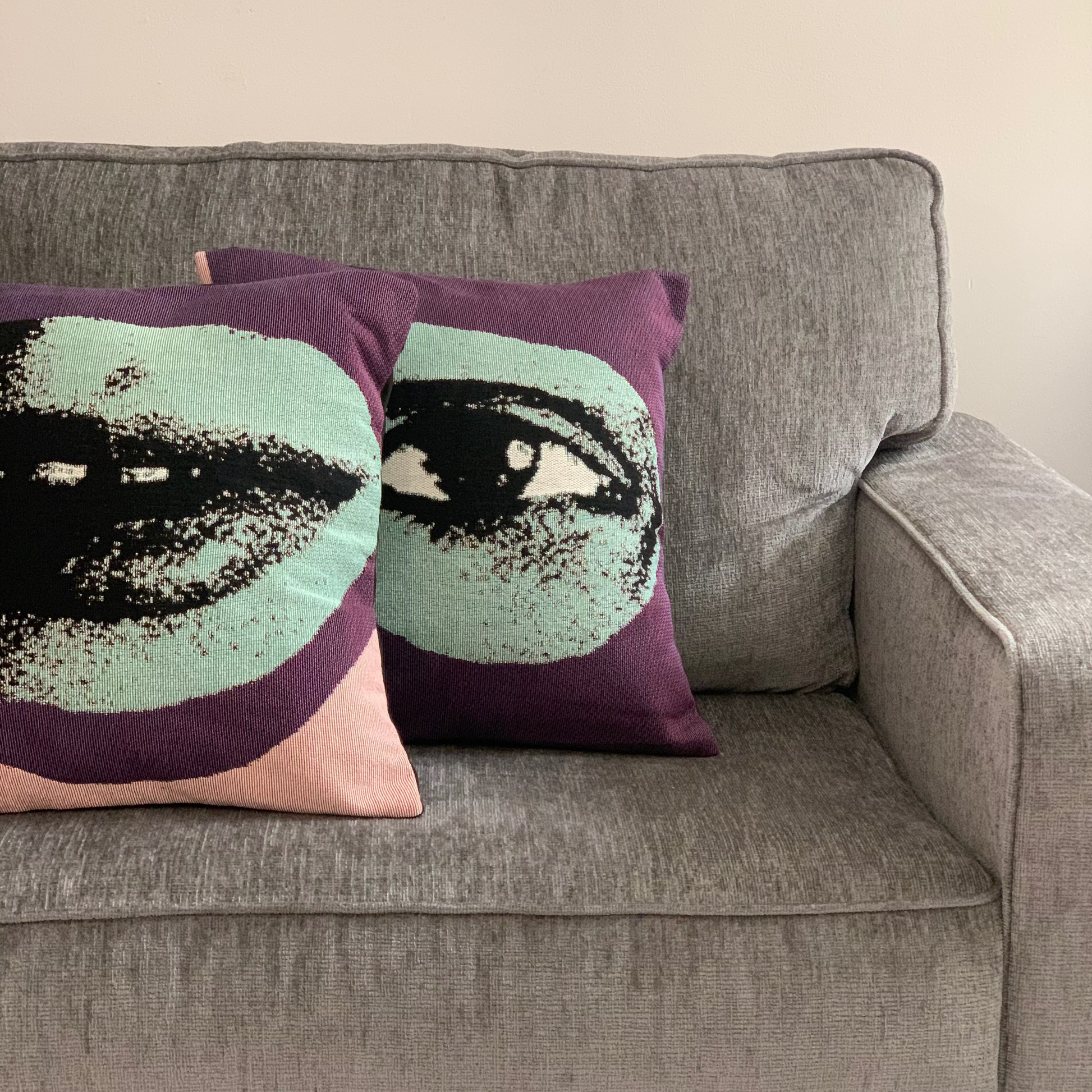Two decorative pillows with face designs on a gray couch.