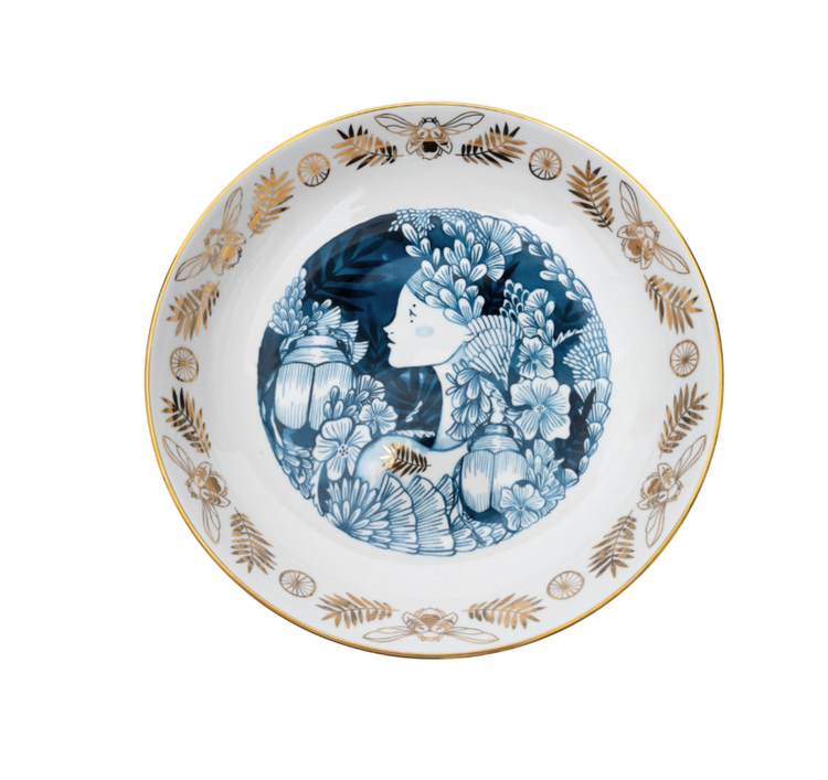 A ceramic serving bowl with a detailed illustration of a garden scene, featuring blue plants and gold accents on a white background.