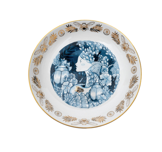 A ceramic serving bowl with a detailed illustration of a garden scene, featuring blue plants and gold accents on a white background.
