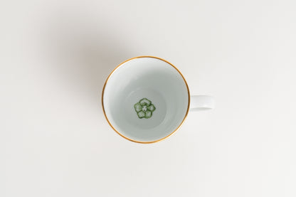 White teacup with gold rim and green floral design on a light gray background