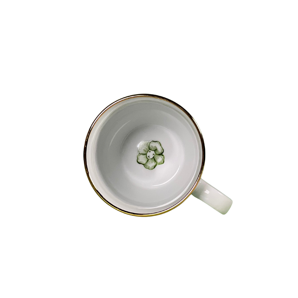 White mug with gold rim and green floral design on a white background